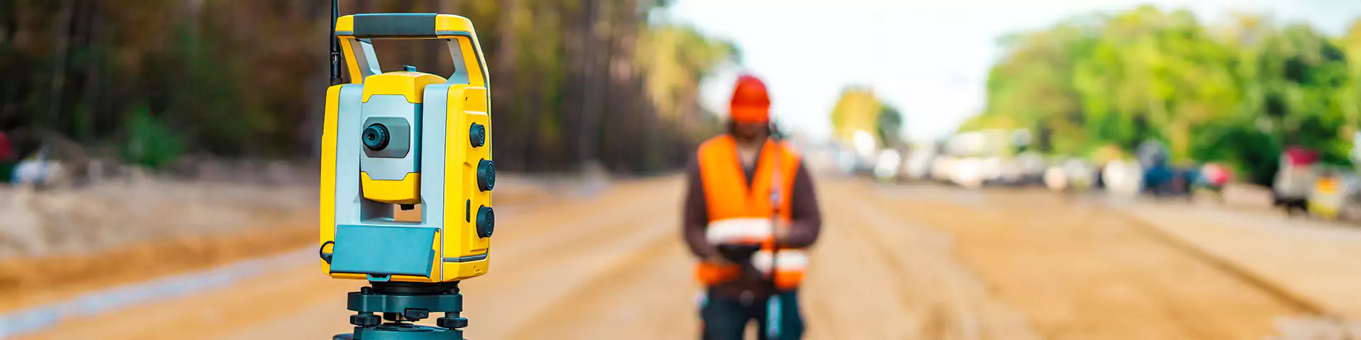 Vermessungsingenieur mit Ausrüstung auf einer Straße mit Baumaschinen und Baustelle im Hintergrund